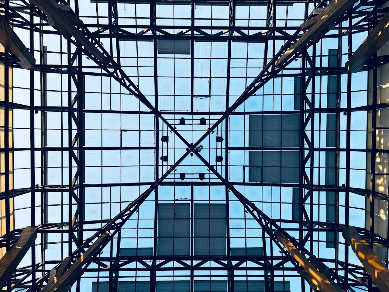 A striking view of a glass atrium ceiling framed with steel structures and visible blue sky.