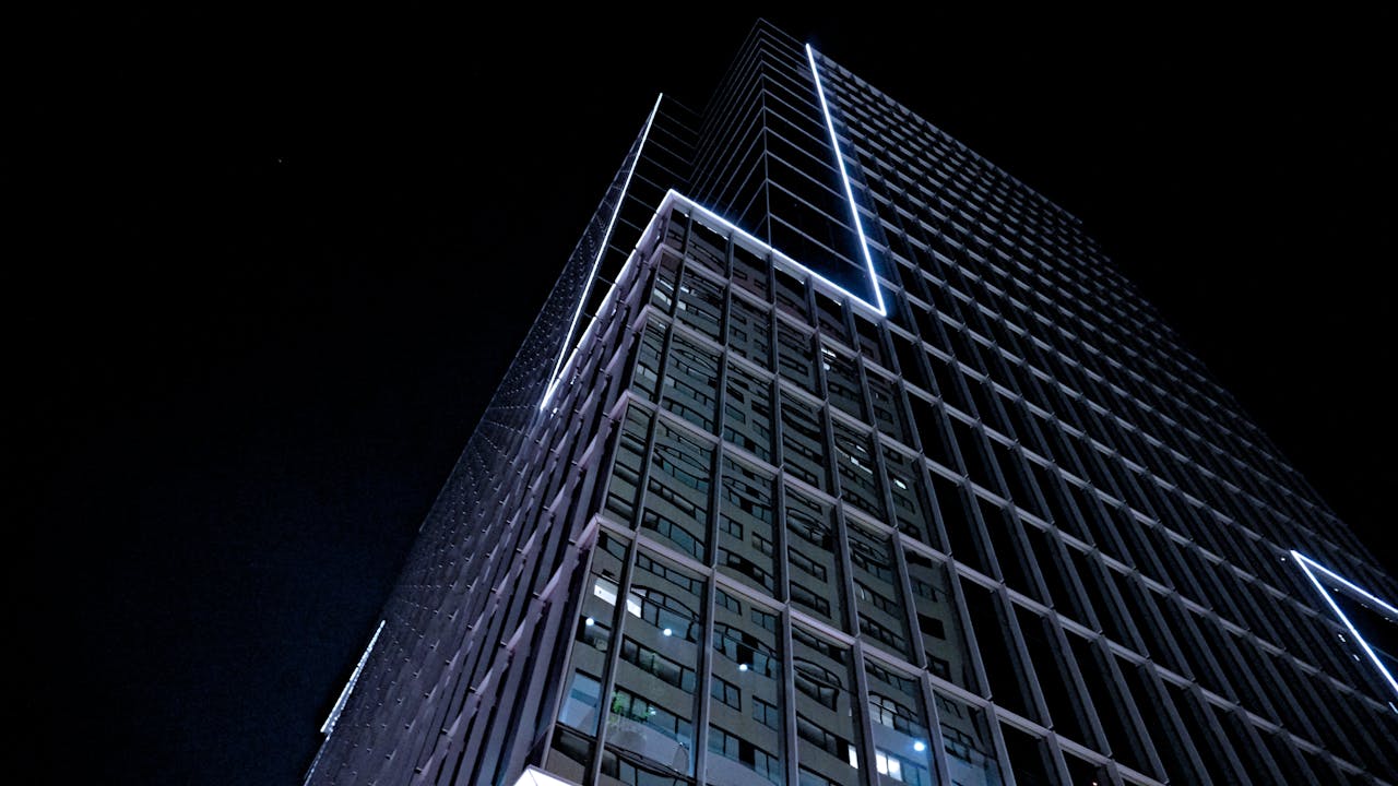 Modern skyscraper with geometric facade illuminated at night, showcasing urban architecture.